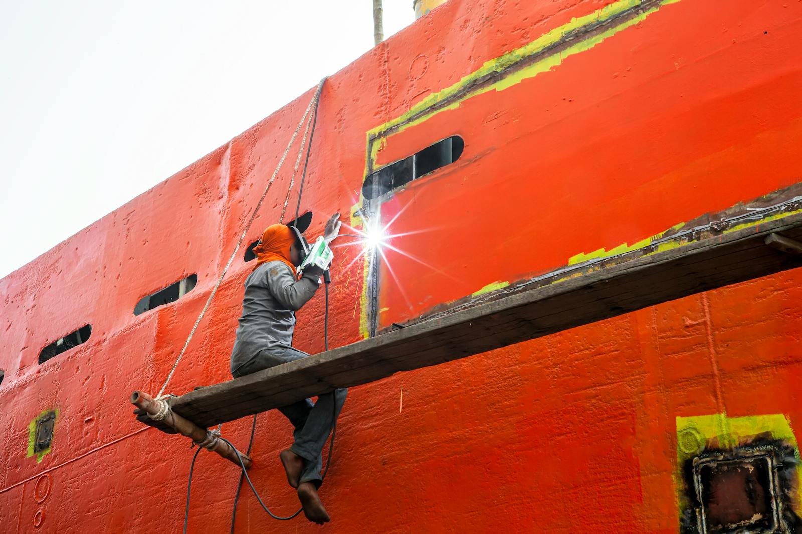A man welding on a large orange ship